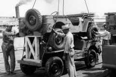 Original caption: \"Side view of stacked (double-decked) trucks, 1/4 ton 4x4, on Pier 2, HRPE, before being placed on Liberty Ship Esek Hopkins (HR-438). Official Photograph U.S. Army Signal Corps, Hampton Roads Port of Embarkation, Newport News Virginia.\"